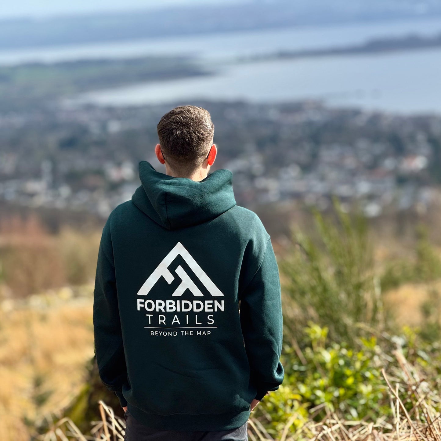 Person wearing a hoodie with 'Forbidden Trails' logo overlooking a scenic landscape.