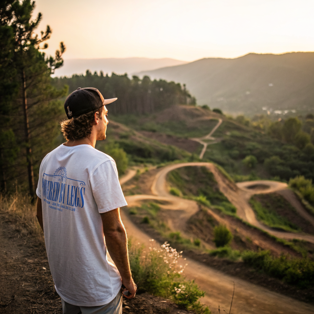 Man in a white t-shirt and cap overlooking a winding dirt track with a white tshirt on with text 'powered by legs'