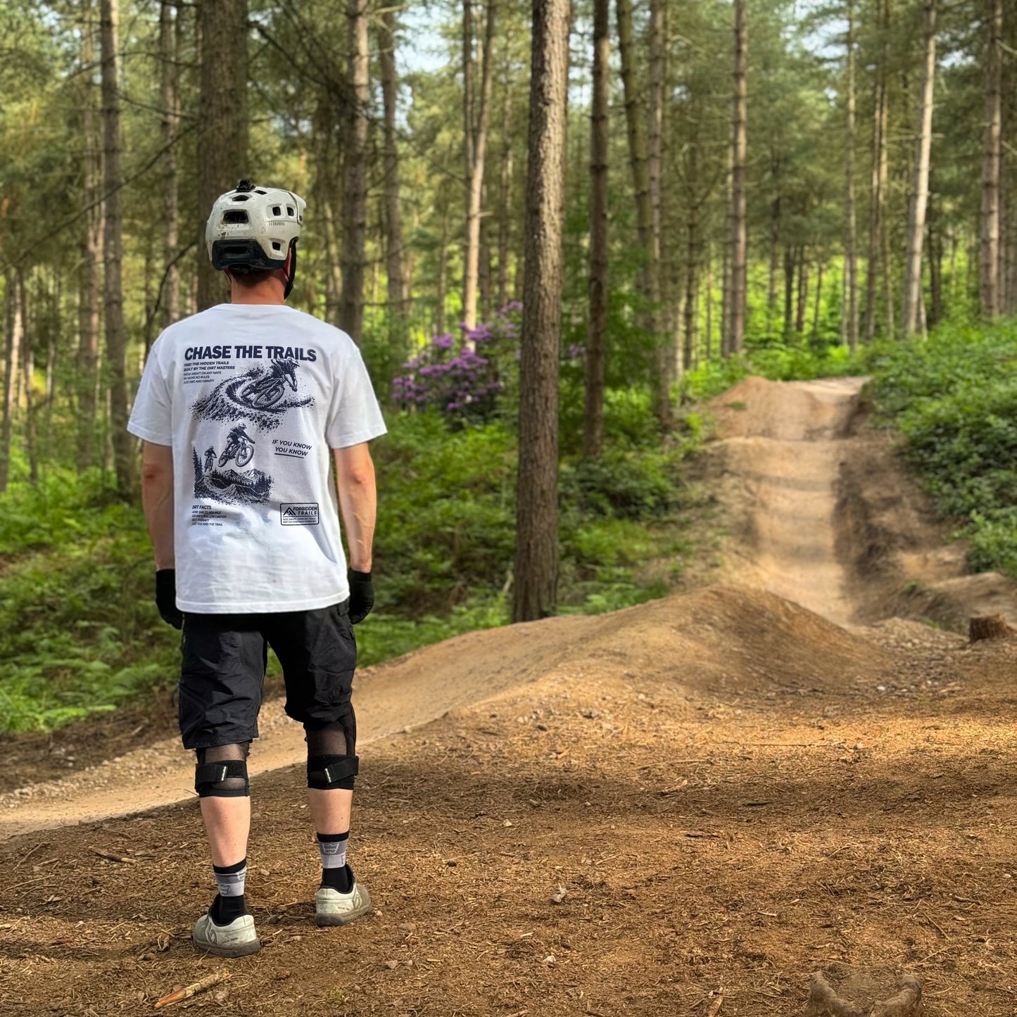 Person on a mountain bike trail in a forest wearing a helmet and protective gear.