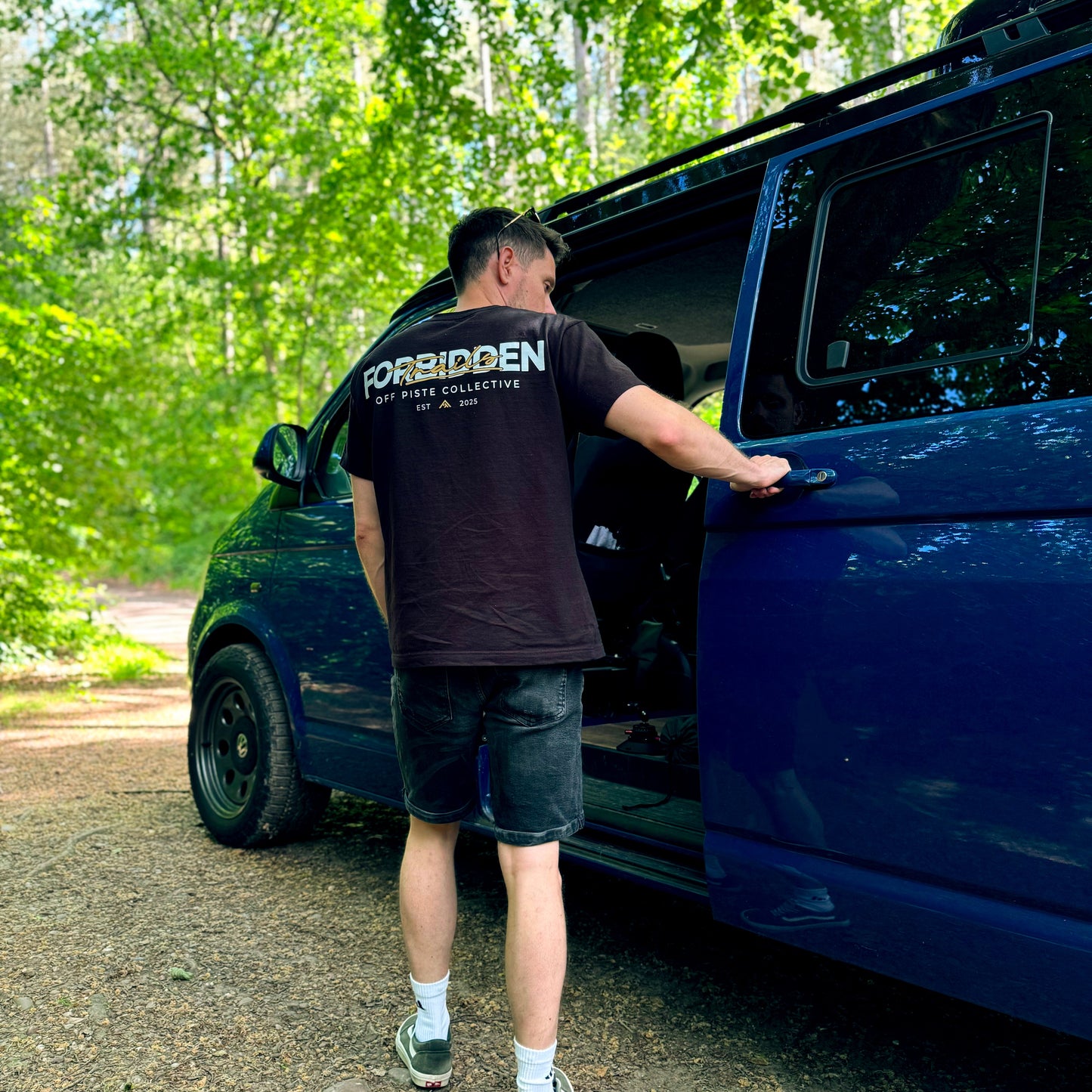 Man opening the door of a blue van in a forested area