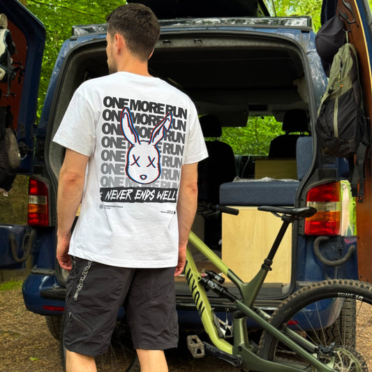 Man with a bicycle leaning against an van, wearing a white t-shirt with text and graphics.