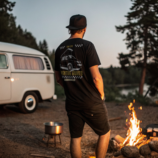 Man standing by a campfire with a vintage van in a forest setting