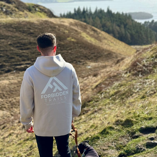 Person wearing a hoodie with 'Forbidden Trails' logo walking on a grassy hillside.