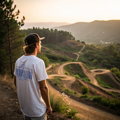 Man in a white t-shirt and cap overlooking a winding dirt track with a white tshirt on with text 'powered by legs'