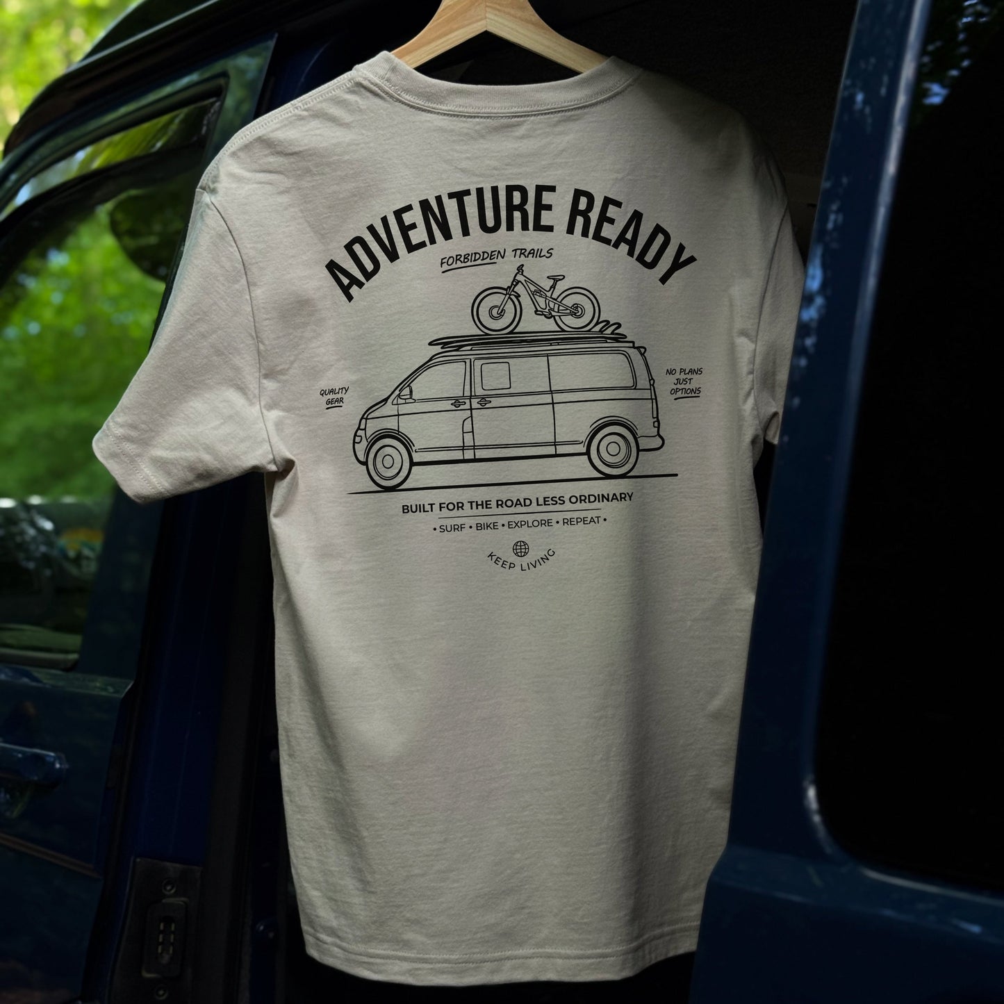 Beige t-shirt with 'Adventure Ready' graphic hanging from a van