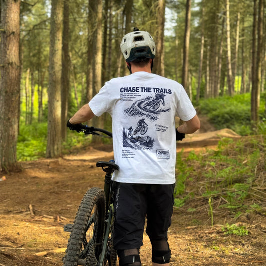 Person with a mountain bike in a forest wearing a white t-shirt with graphics and text.
