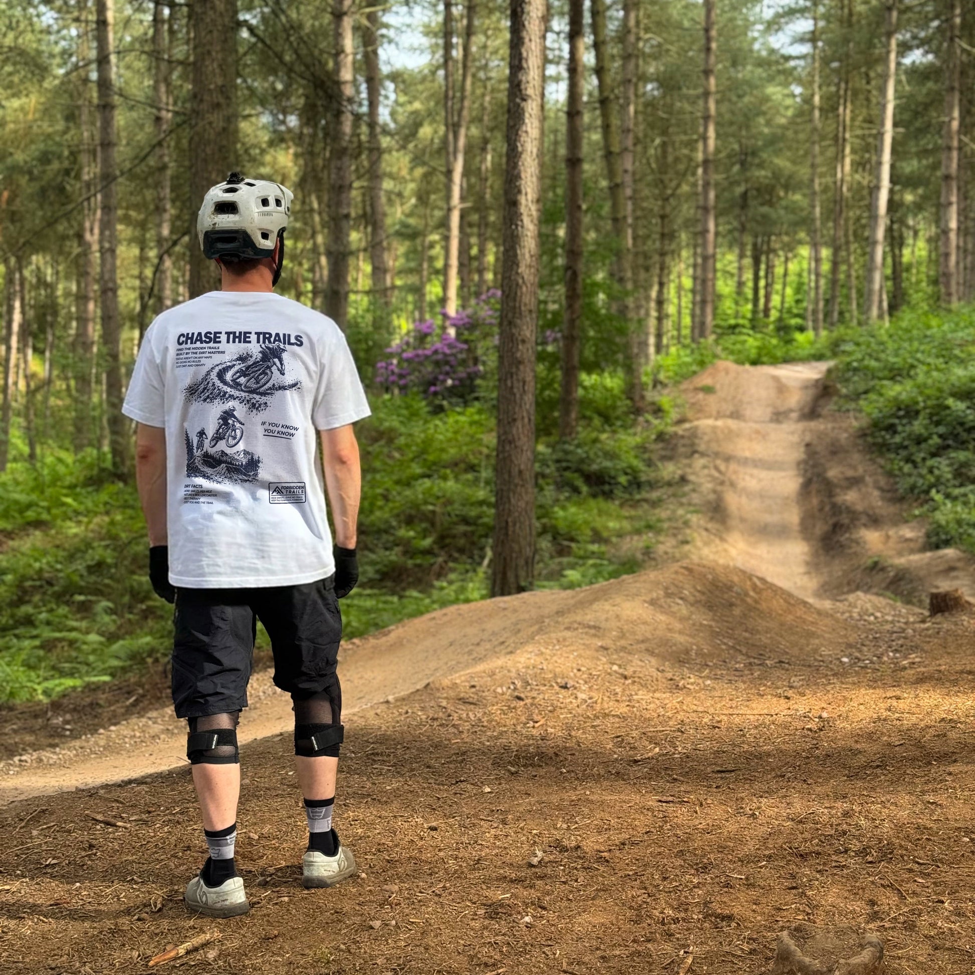 Person on a mountain bike trail in a forest wearing a helmet and protective gear.