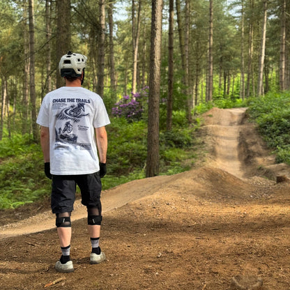 Person on a mountain bike trail in a forest wearing a helmet and protective gear.