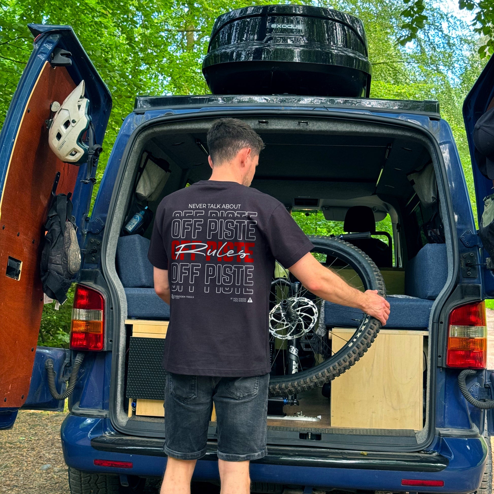 Person taking a bike out of a van wearing a black tee with  graphic on the back