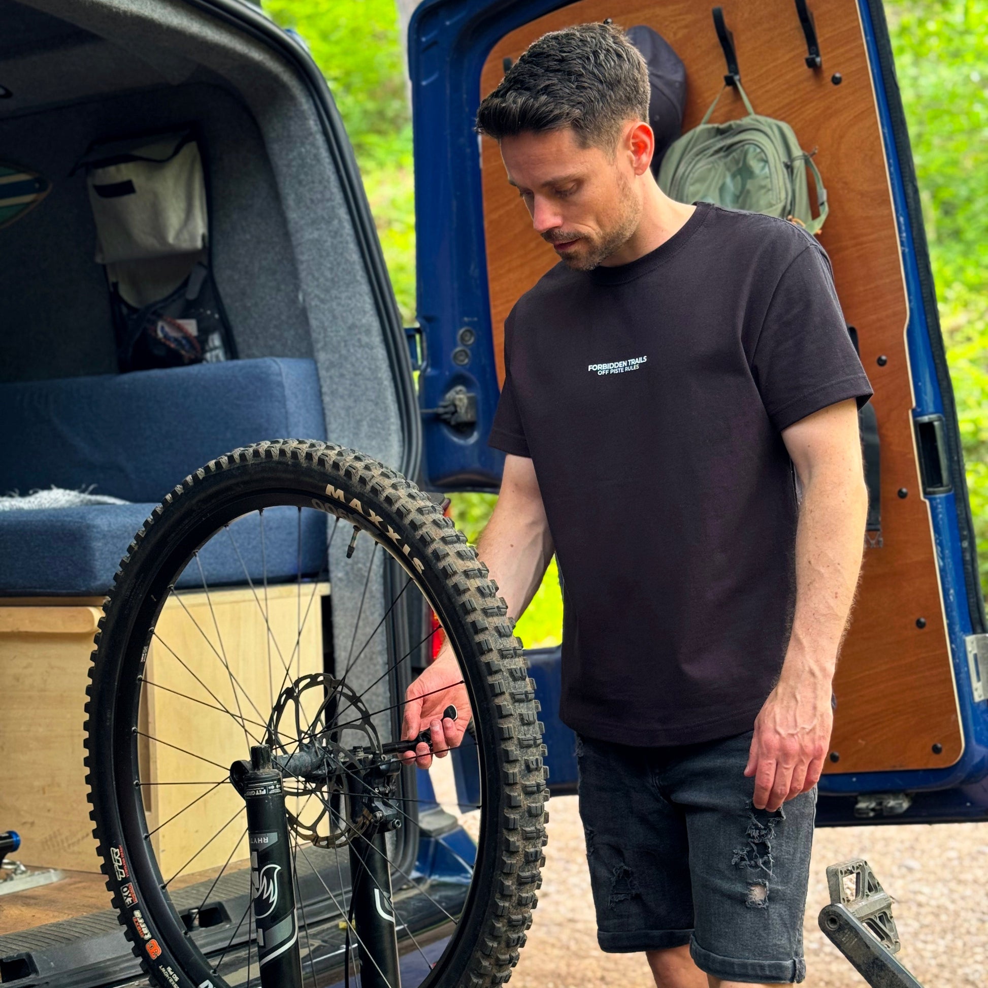 Man loading a bicycle onto a van with a forest background