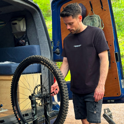 Man loading a bicycle onto a van with a forest background