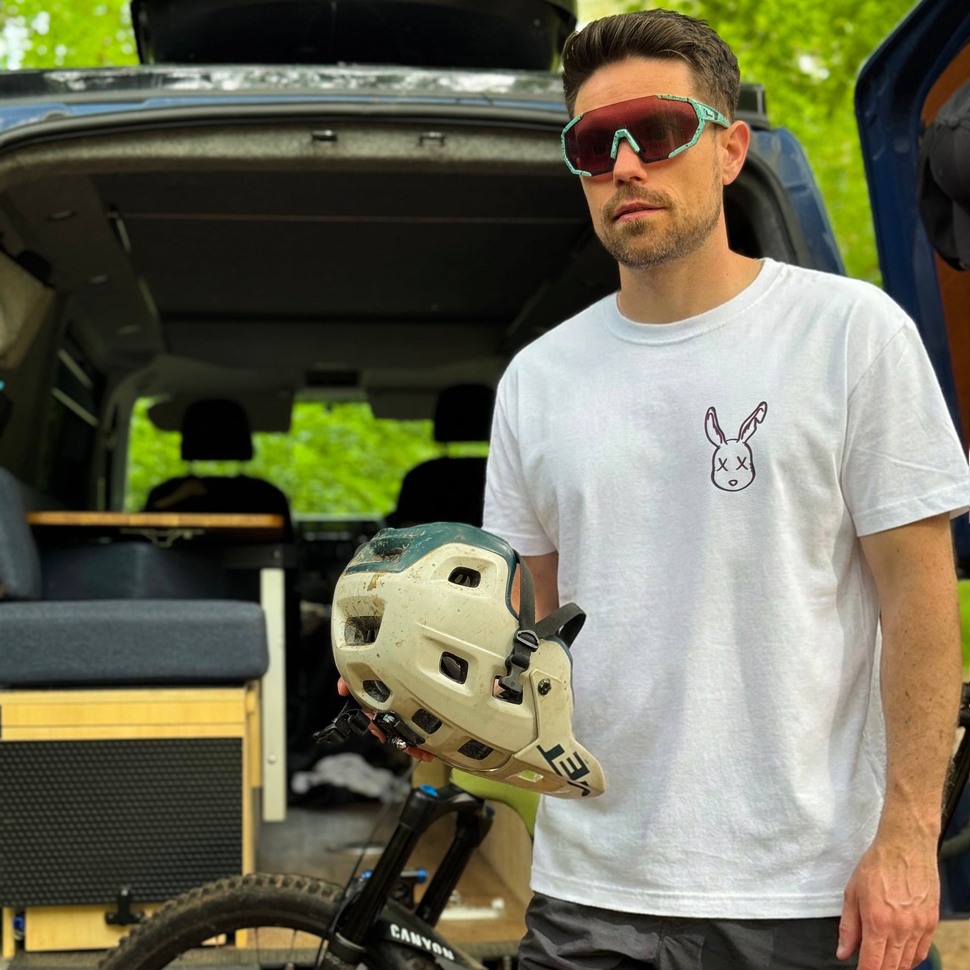 Man holding a helmet next to an open vehicle with camping gear