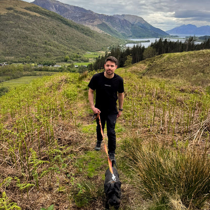 man walking up hill with dog mountain and lakes in the background